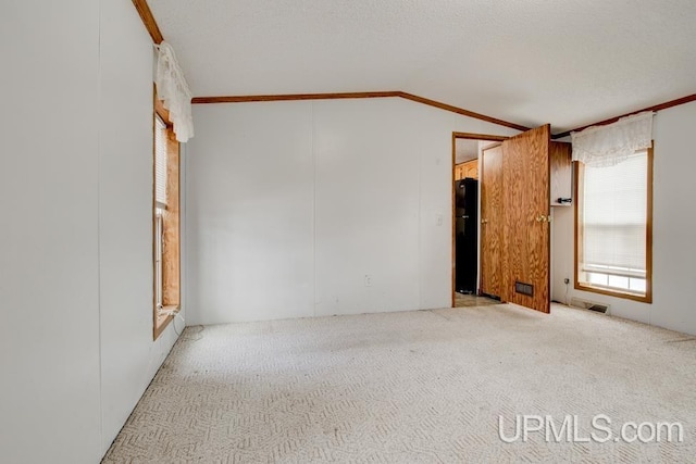 carpeted empty room with ornamental molding, vaulted ceiling, and a textured ceiling