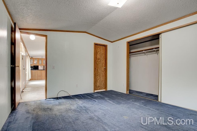 unfurnished bedroom with lofted ceiling, dark carpet, ornamental molding, and a closet