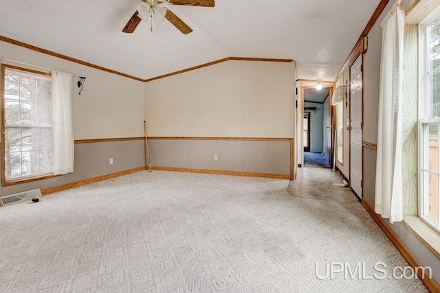 carpeted spare room featuring ceiling fan, a healthy amount of sunlight, ornamental molding, and vaulted ceiling