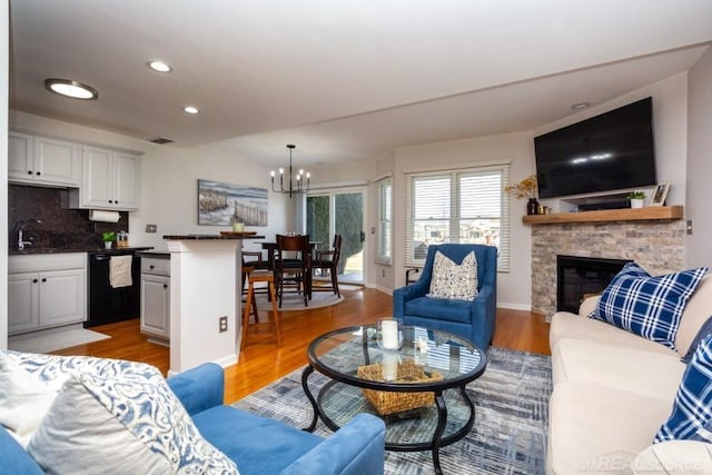 living room with a notable chandelier, sink, a fireplace, and light hardwood / wood-style floors