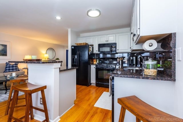 kitchen with black appliances, sink, white cabinets, a kitchen breakfast bar, and kitchen peninsula