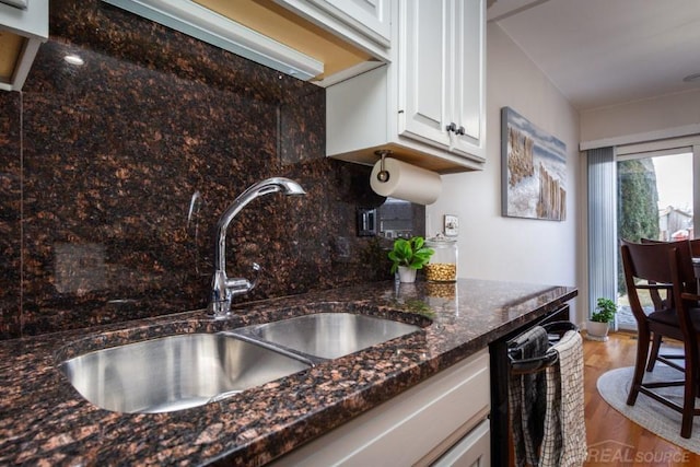 kitchen with sink, black dishwasher, dark stone counters, decorative backsplash, and white cabinets