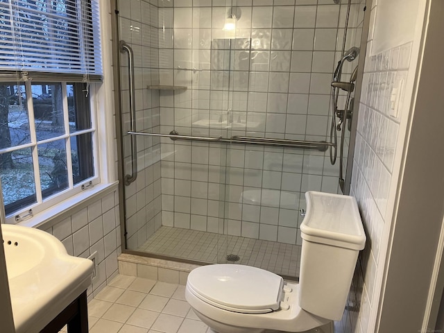 bathroom with tile patterned floors, toilet, tile walls, vanity, and a shower with door