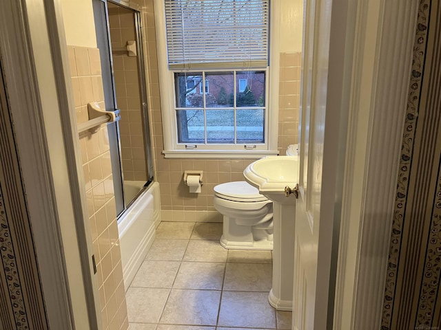 bathroom with tile patterned flooring, enclosed tub / shower combo, tile walls, and toilet