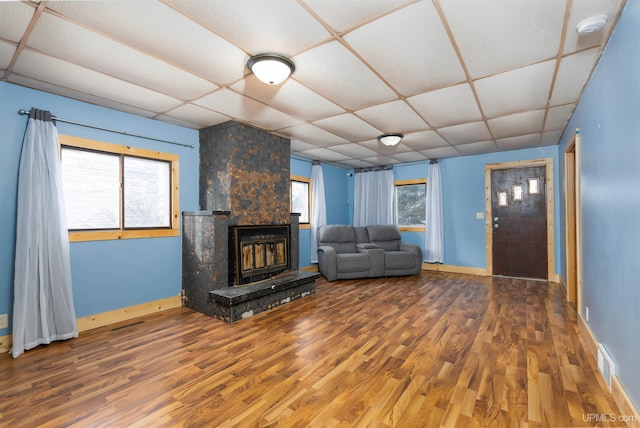 unfurnished living room with a large fireplace, wood-type flooring, a healthy amount of sunlight, and a drop ceiling