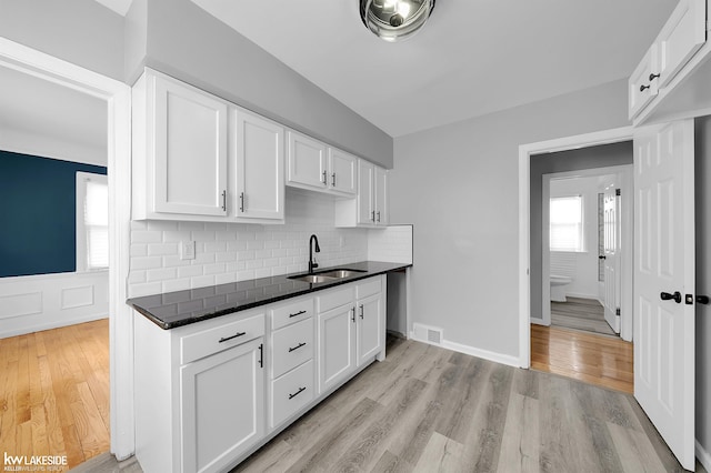 kitchen featuring tasteful backsplash, white cabinetry, sink, and light hardwood / wood-style floors