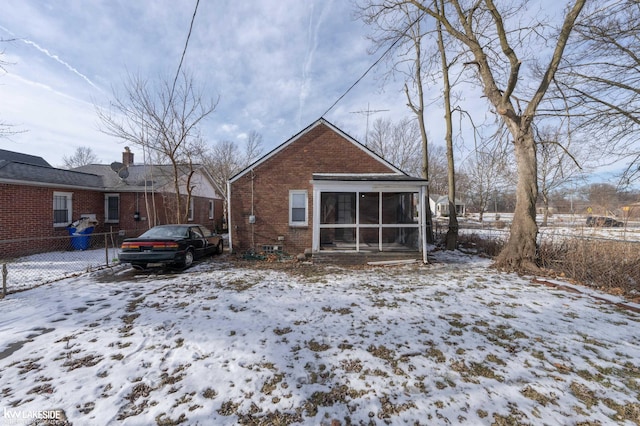 snow covered rear of property with a sunroom