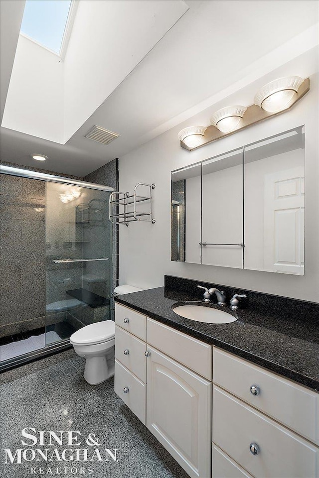 bathroom with vanity, a skylight, a shower with door, and toilet