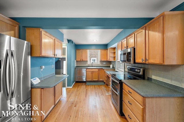 kitchen with appliances with stainless steel finishes, sink, backsplash, and light wood-type flooring