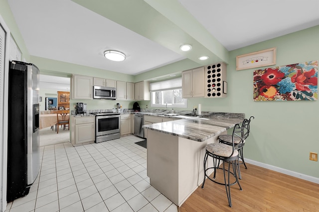 kitchen featuring sink, light tile patterned floors, a breakfast bar area, appliances with stainless steel finishes, and kitchen peninsula