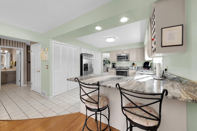 kitchen featuring sink, a breakfast bar area, kitchen peninsula, stainless steel appliances, and light stone countertops