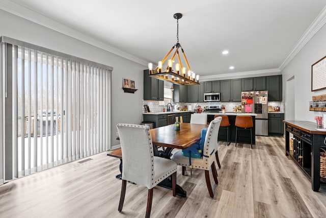 dining area featuring crown molding, sink, an inviting chandelier, and light wood-type flooring