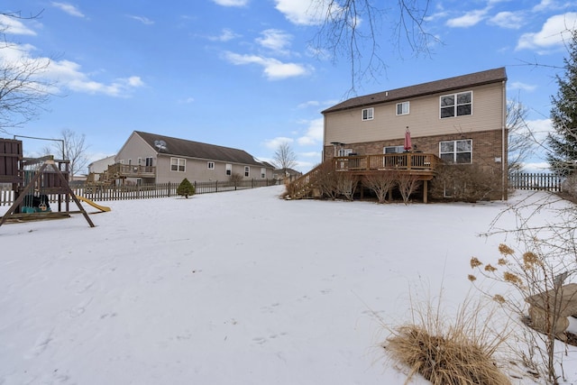 snow covered rear of property featuring a playground and a wooden deck