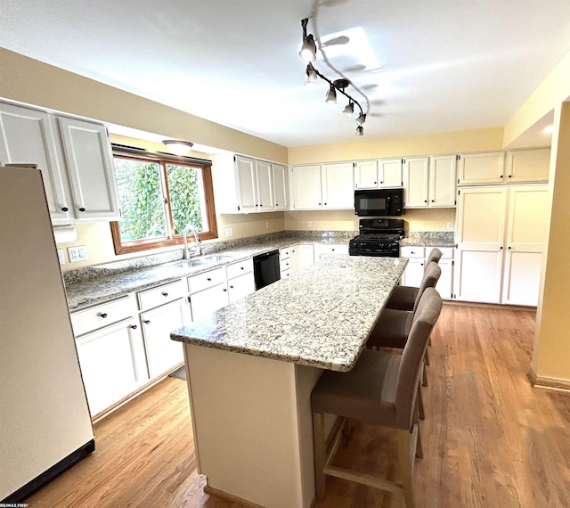 kitchen featuring a breakfast bar, black appliances, a kitchen island, light stone countertops, and white cabinets