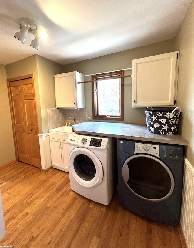 clothes washing area featuring cabinets, sink, washer and dryer, and light hardwood / wood-style flooring