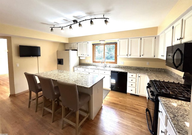 kitchen with a center island, light wood-type flooring, a kitchen breakfast bar, light stone countertops, and black appliances