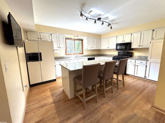 kitchen with a kitchen bar, white cabinetry, a kitchen island, light stone countertops, and black appliances