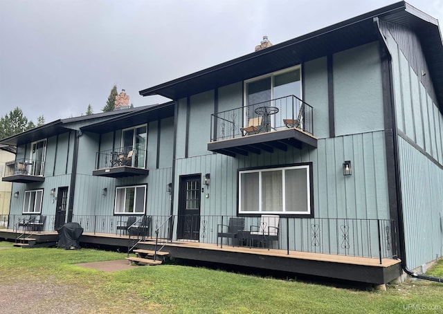 rear view of house featuring a balcony, a deck, and a lawn