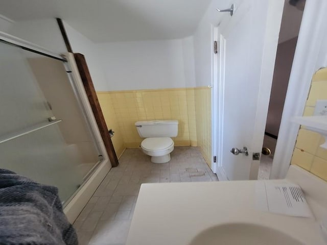 bathroom featuring a shower with door, tile walls, and toilet