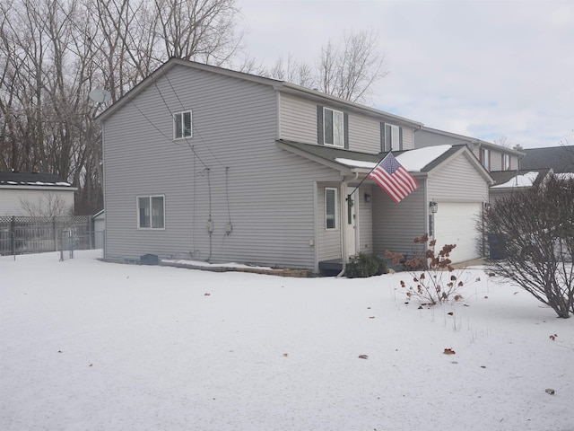 snow covered house with a garage and fence