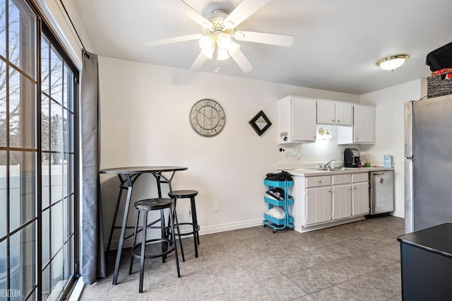 kitchen with appliances with stainless steel finishes, sink, white cabinets, a kitchen bar, and ceiling fan