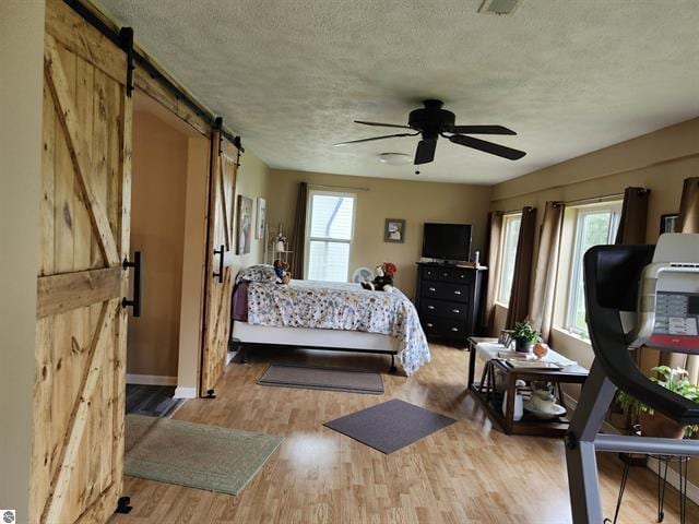 bedroom featuring a barn door, light hardwood / wood-style floors, and a textured ceiling