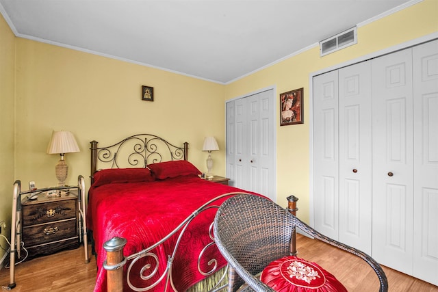 bedroom featuring hardwood / wood-style flooring, crown molding, and two closets