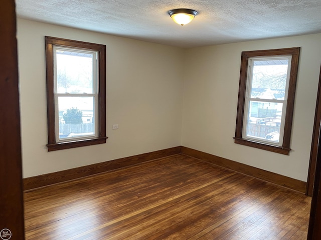 spare room featuring dark wood-type flooring, a healthy amount of sunlight, and a textured ceiling