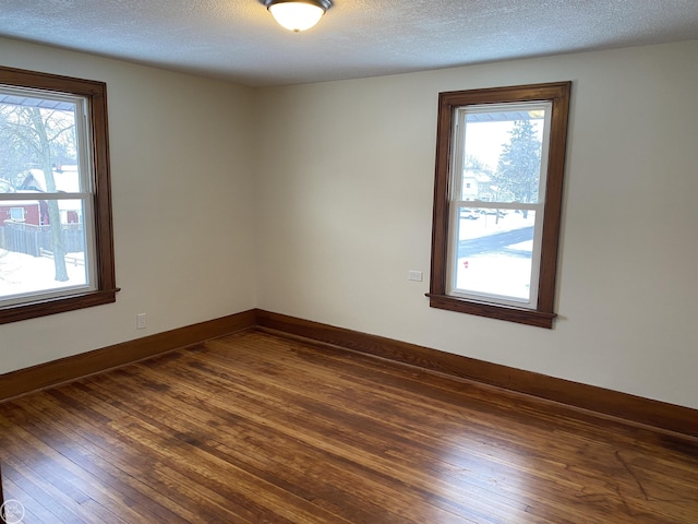 empty room with dark wood-type flooring, plenty of natural light, and a textured ceiling