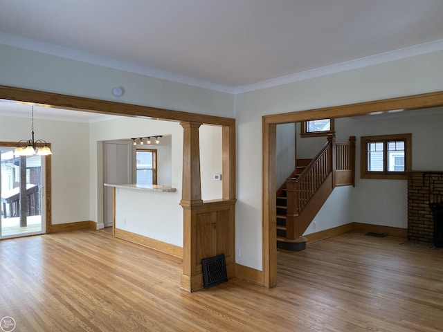 unfurnished living room featuring crown molding, a brick fireplace, a notable chandelier, and light hardwood / wood-style floors