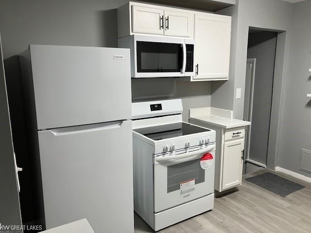 kitchen with white cabinetry, white appliances, and light hardwood / wood-style floors