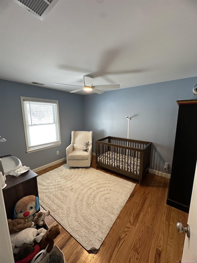 bedroom with wood-type flooring, a nursery area, and ceiling fan