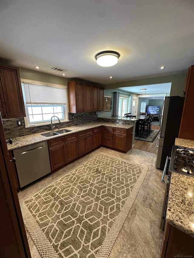 kitchen featuring sink, appliances with stainless steel finishes, kitchen peninsula, light stone countertops, and backsplash