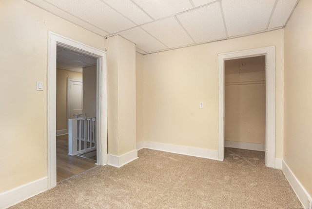 unfurnished bedroom with a walk in closet, a closet, light carpet, and a drop ceiling