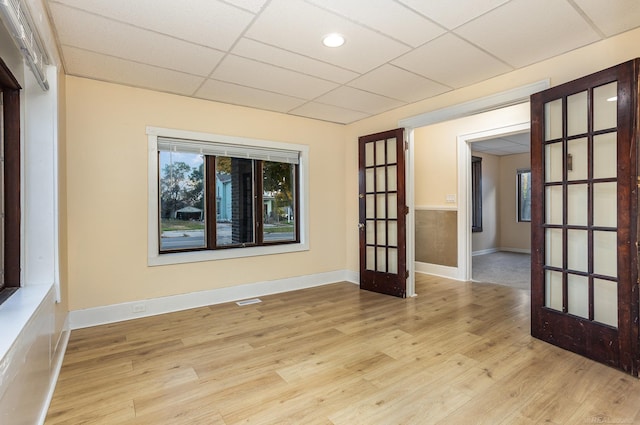 empty room with french doors, light wood-type flooring, and a drop ceiling