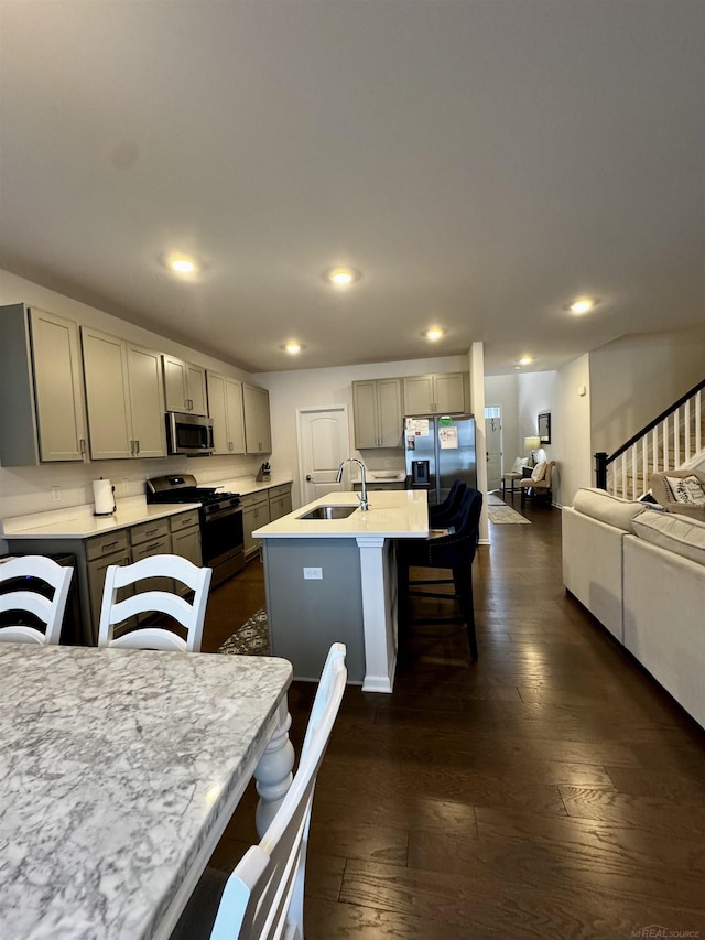 kitchen with dark wood-type flooring, sink, gray cabinetry, a center island with sink, and appliances with stainless steel finishes