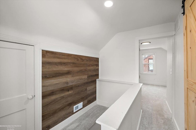 hall featuring carpet floors, vaulted ceiling, a barn door, and wood walls