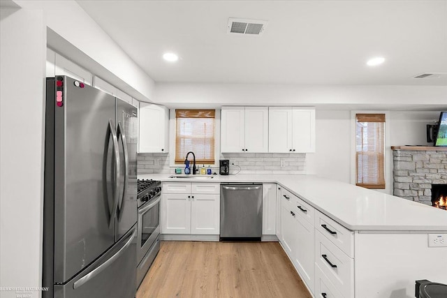 kitchen with appliances with stainless steel finishes, kitchen peninsula, sink, and white cabinets