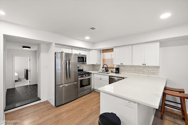 kitchen featuring white cabinetry, a kitchen bar, kitchen peninsula, stainless steel appliances, and light wood-type flooring