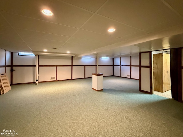 basement with a paneled ceiling and light colored carpet