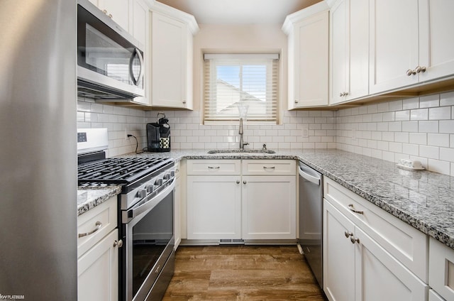 kitchen featuring a sink, white cabinetry, stainless steel appliances, light wood-type flooring, and backsplash