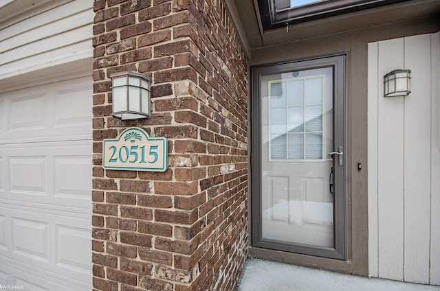 entrance to property featuring a garage and brick siding