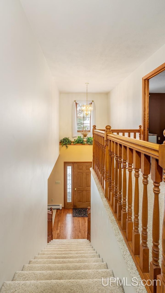 stairs with wood-type flooring, a baseboard radiator, a chandelier, and a high ceiling