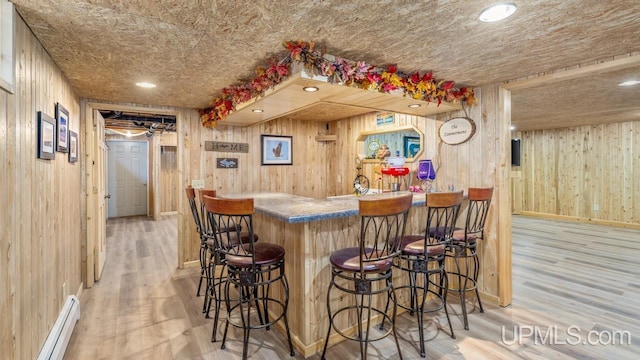 bar with hardwood / wood-style flooring, a baseboard radiator, and wooden walls