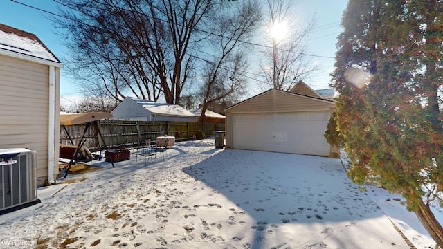 yard layered in snow with a garage, an outdoor structure, cooling unit, and a fire pit