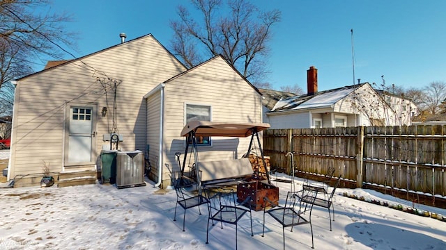 snow covered rear of property featuring central air condition unit and an outdoor fire pit