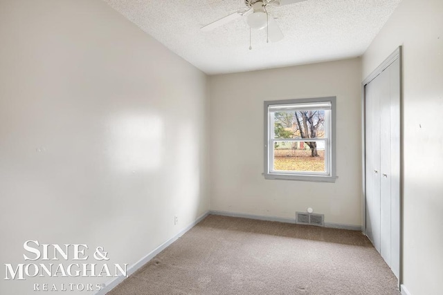 unfurnished bedroom with light carpet, ceiling fan, a closet, and a textured ceiling