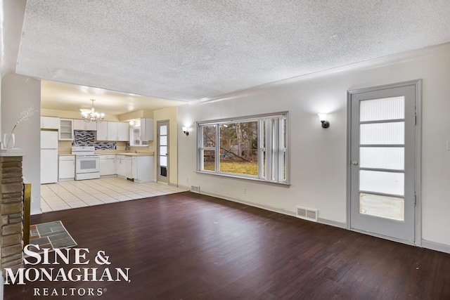 unfurnished living room with an inviting chandelier, a textured ceiling, and light hardwood / wood-style floors