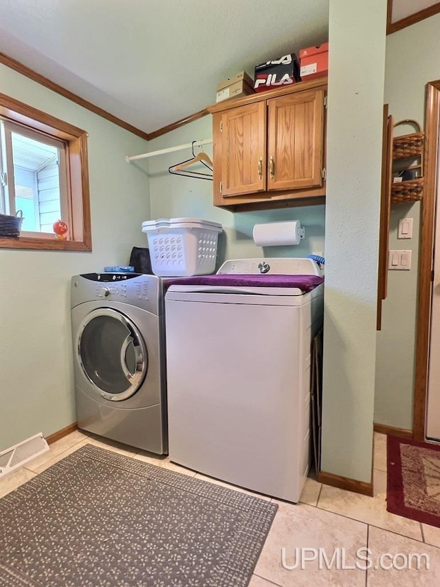 laundry area with separate washer and dryer, light tile patterned floors, ornamental molding, and cabinets