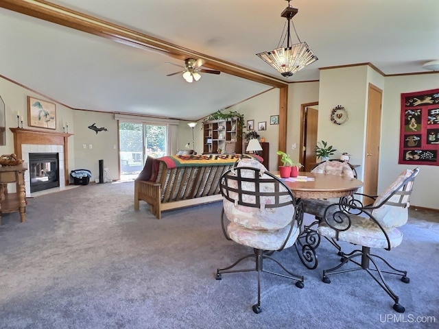 dining area featuring crown molding, ceiling fan, carpet, a tiled fireplace, and vaulted ceiling